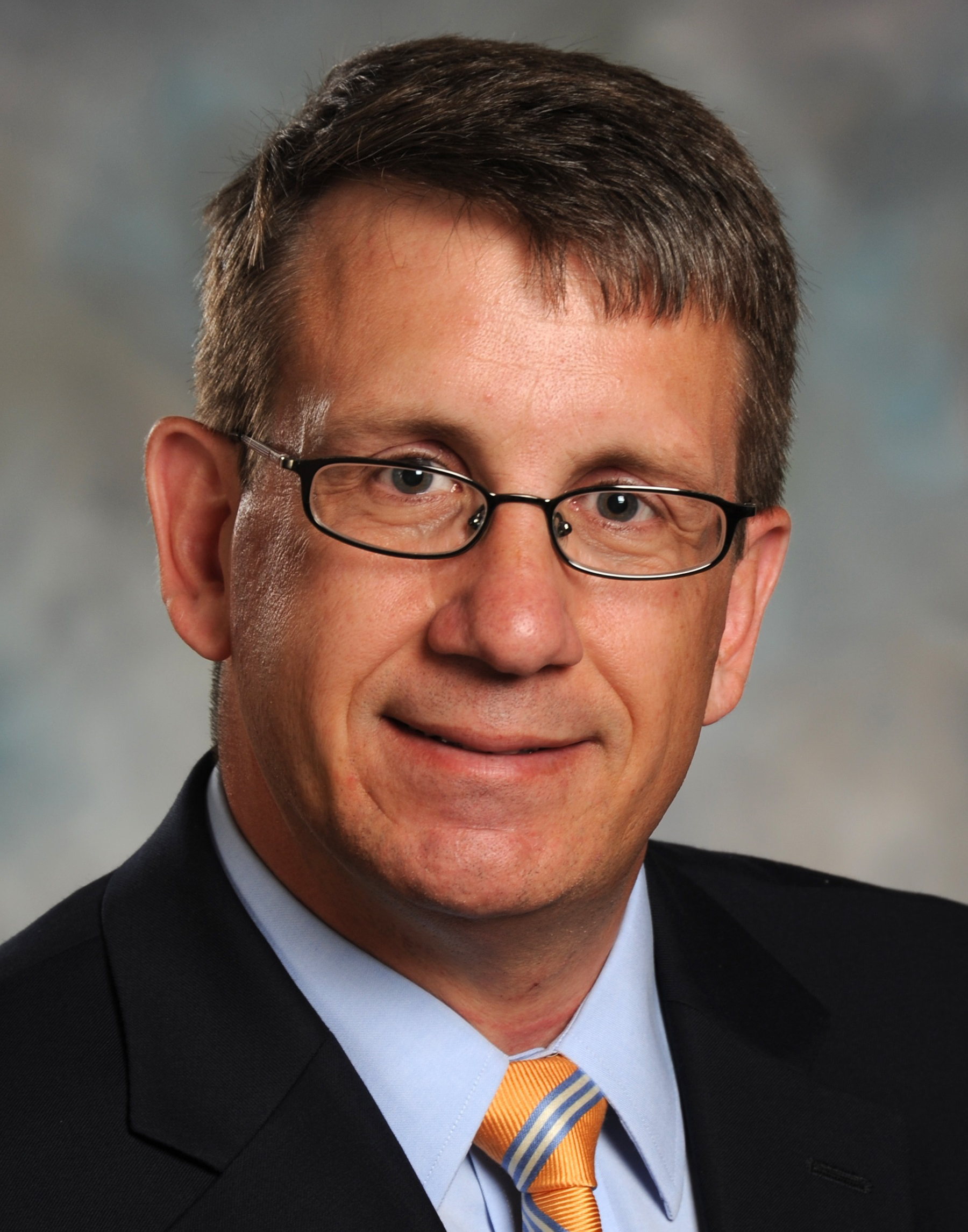 Greg Schuler in glasses on gray background